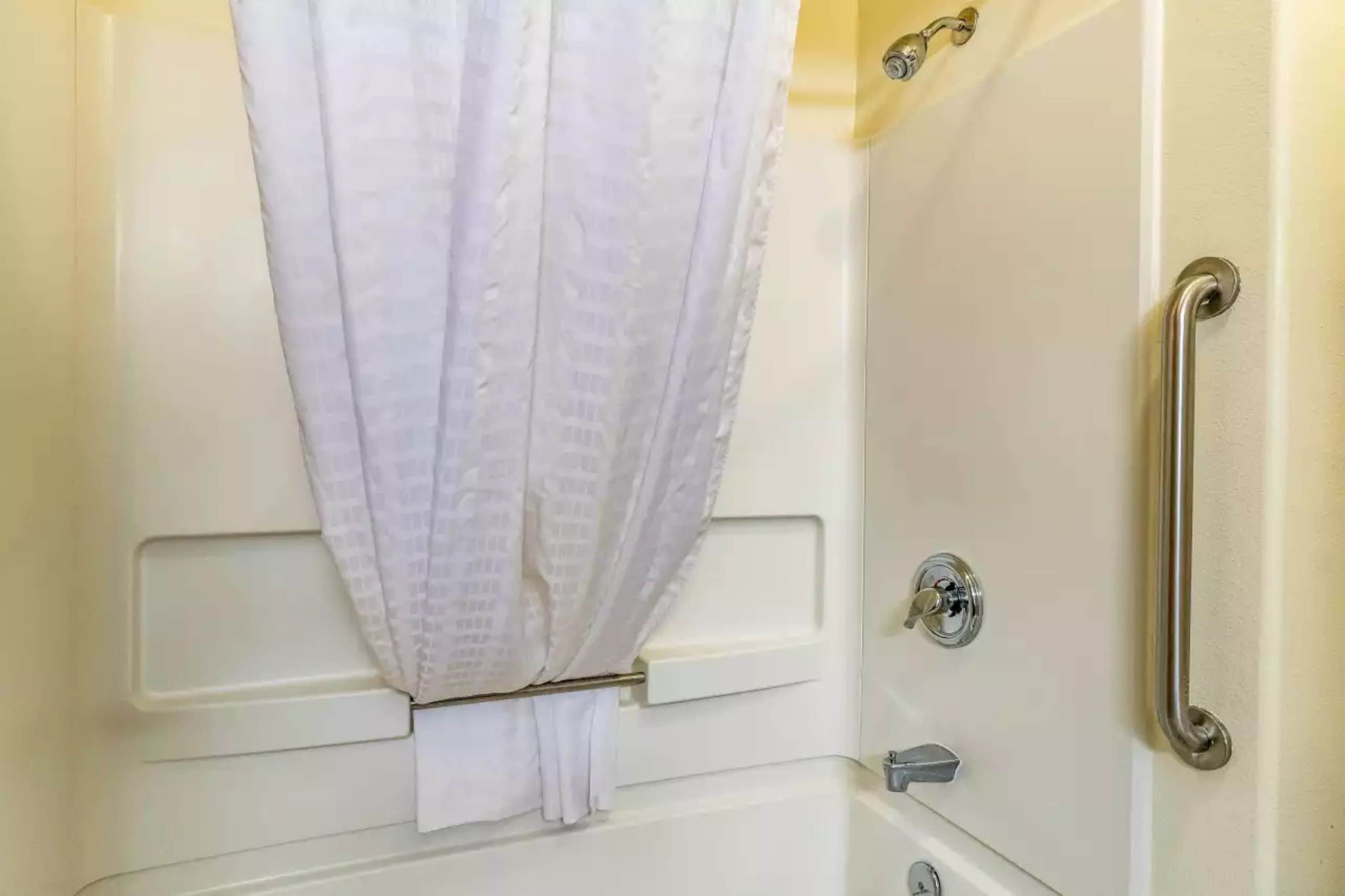 Un baño con una bañera blanca, una cortina de ducha, una barra de apoyo y un perchero.