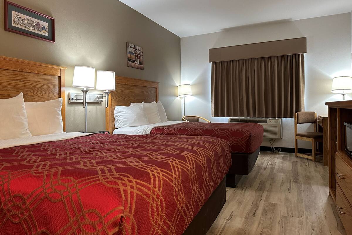 Une chambre d’hôtel avec deux lits, un bureau, une chaise et une fenêtre avec des rideaux.