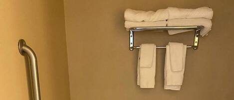 A bathroom with a toilet, handrails, a grab bar, a toilet paper holder, and a step stool.