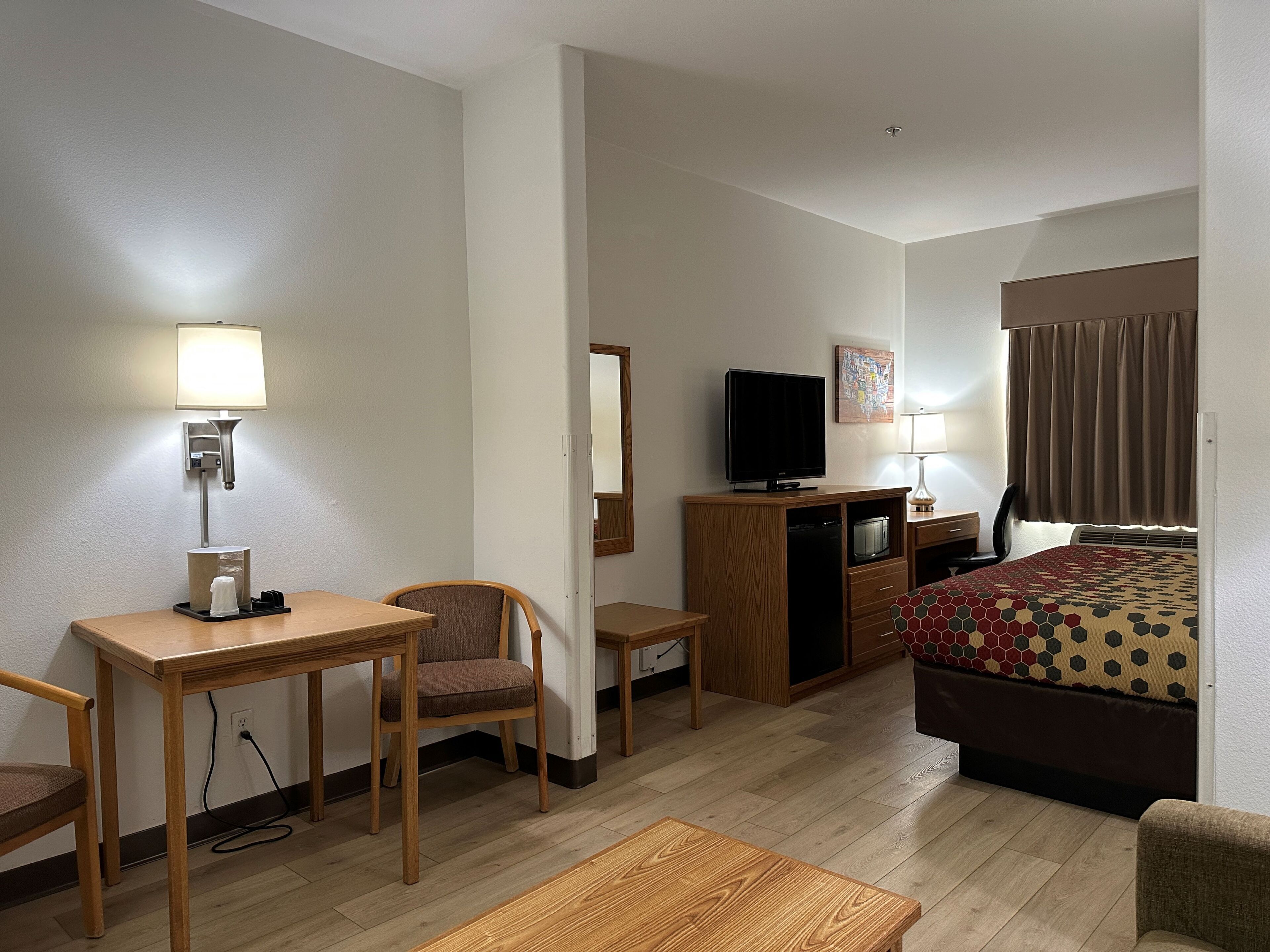 A hotel room with a bed, a desk, a chair, a television, and a lamp.
