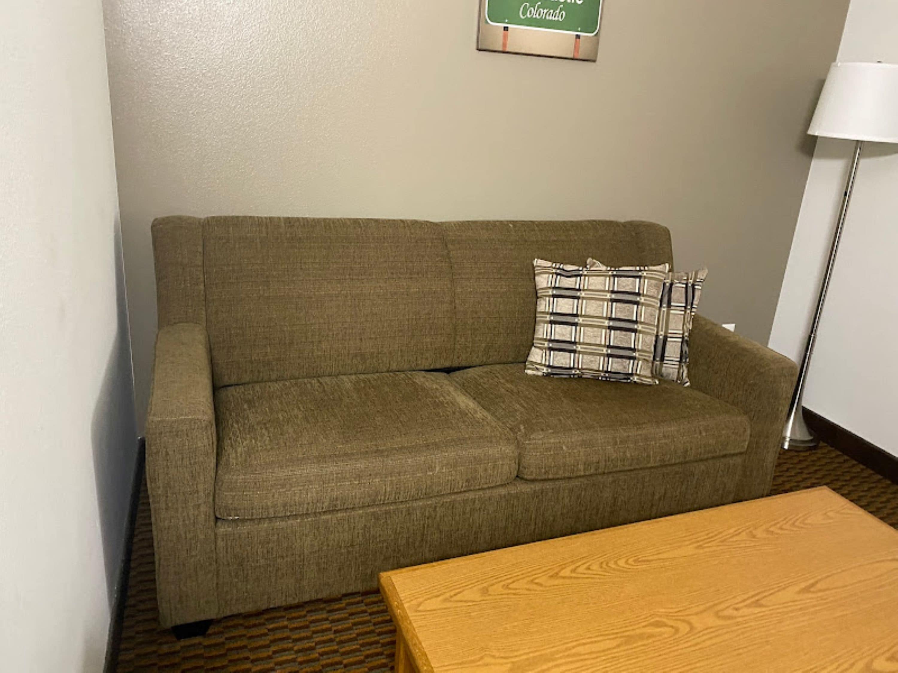 A room with a brown sofa, a plaid pillow, and a wooden table.