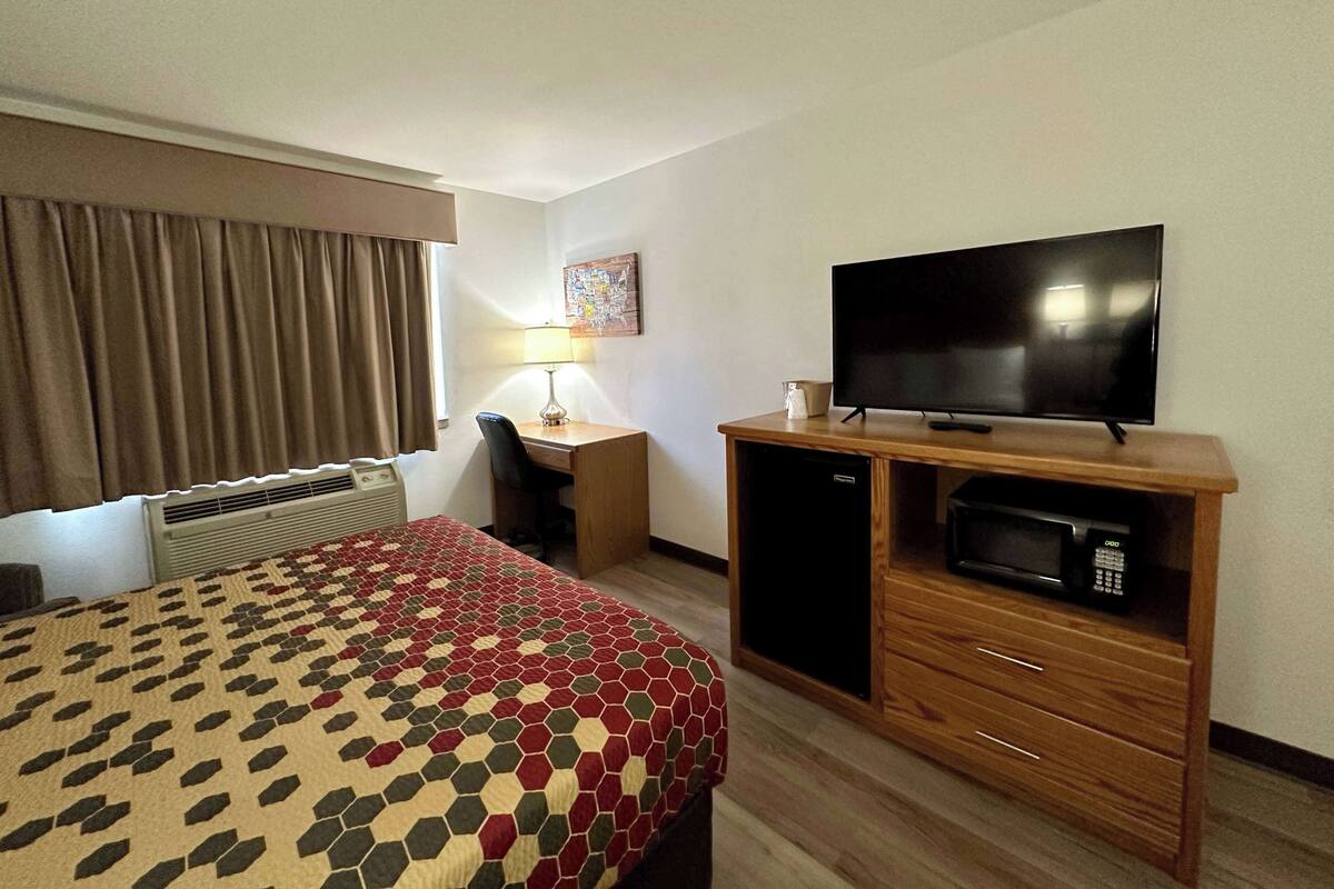 Une chambre d’hôtel équipée d’un lit, d’un bureau, d’une télévision, d’un four à micro-ondes et d’une fenêtre avec des rideaux.