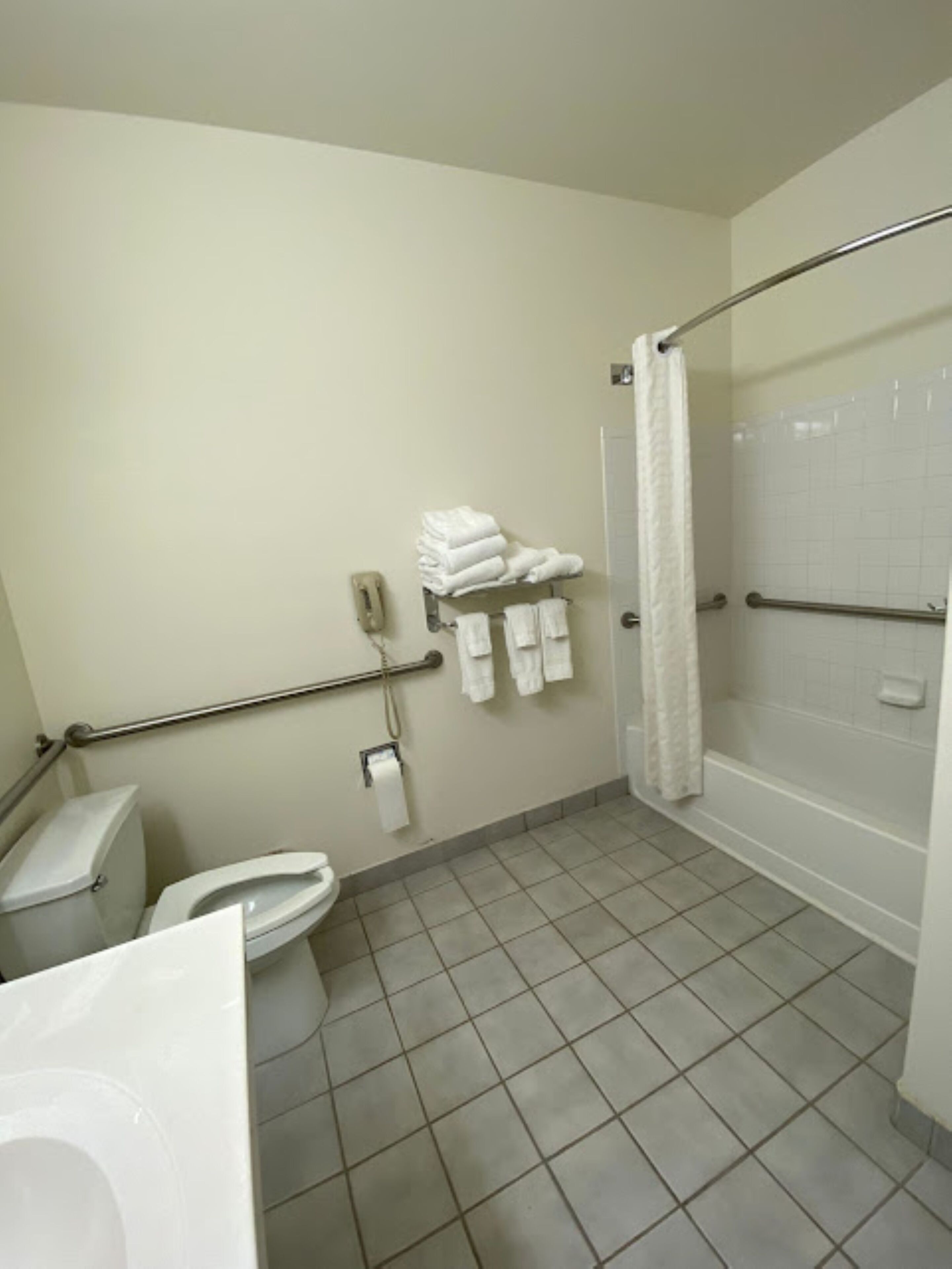 A bathroom with a toilet, a sink, a shower, and a towel rack with folded towels.