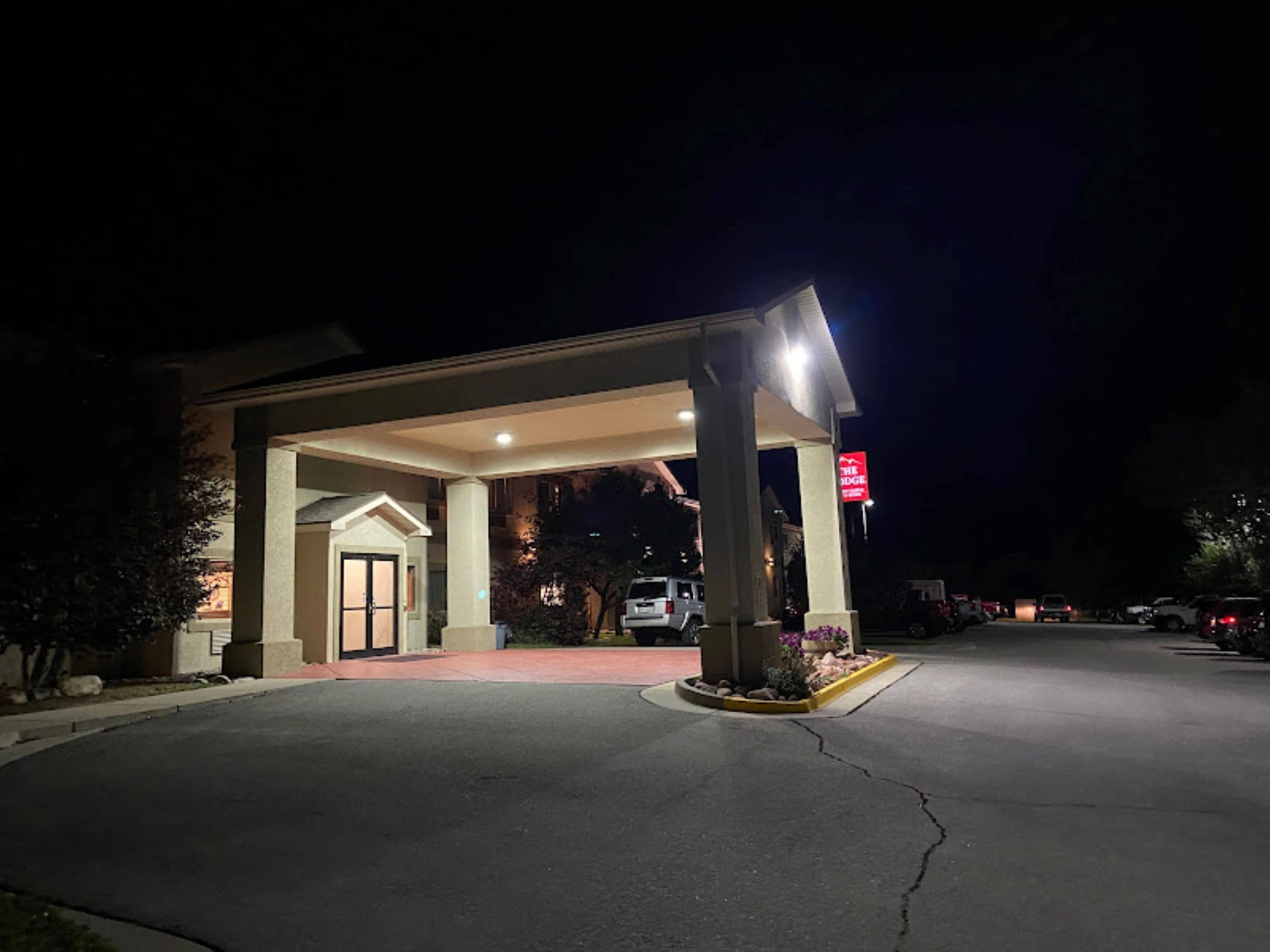 Fachada de hotel de noche con un área techada, un letrero visible y coches estacionados.