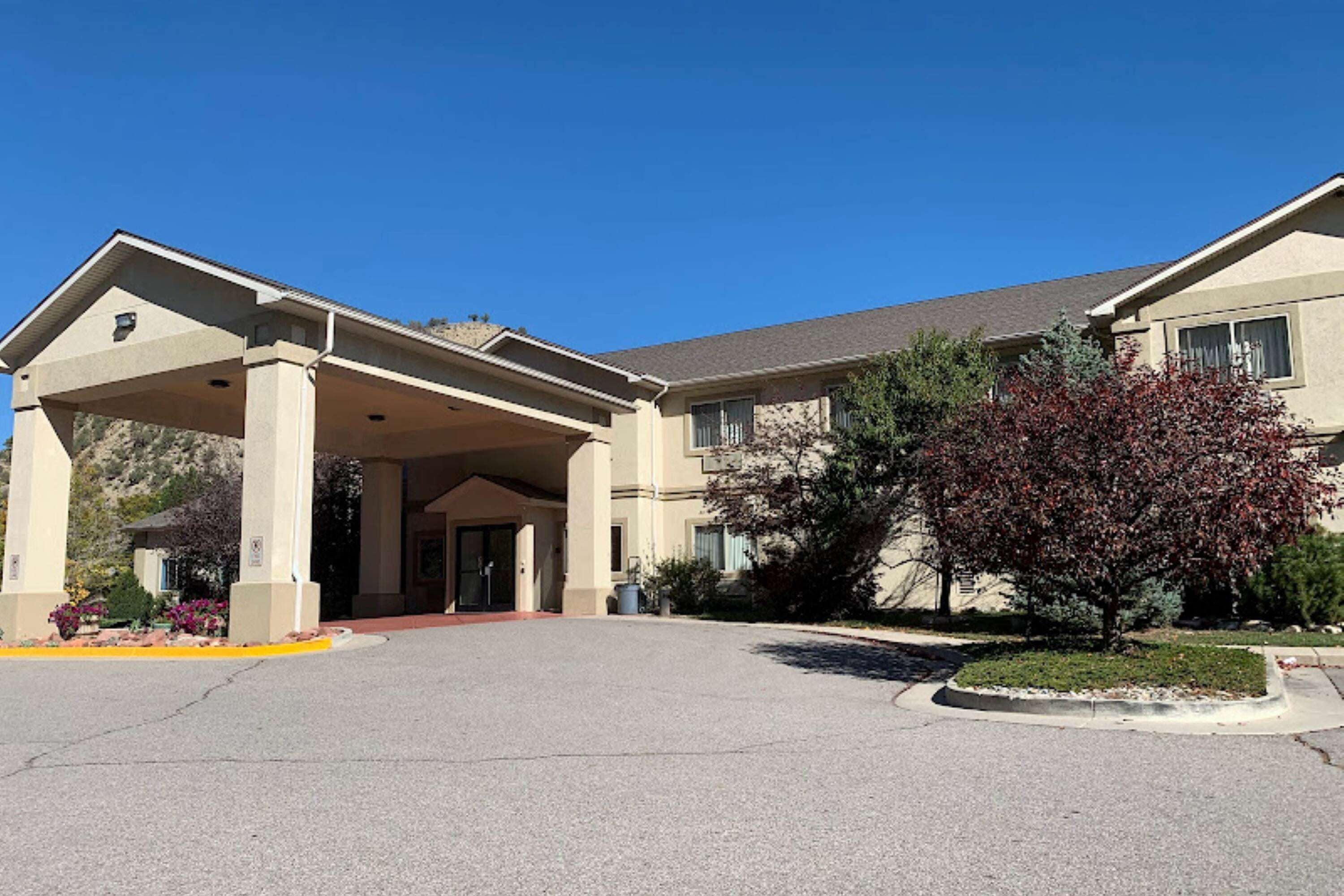 A hotel entrance with a covered driveway, a landscaped garden, and a building with a flat roof and beige exterior.