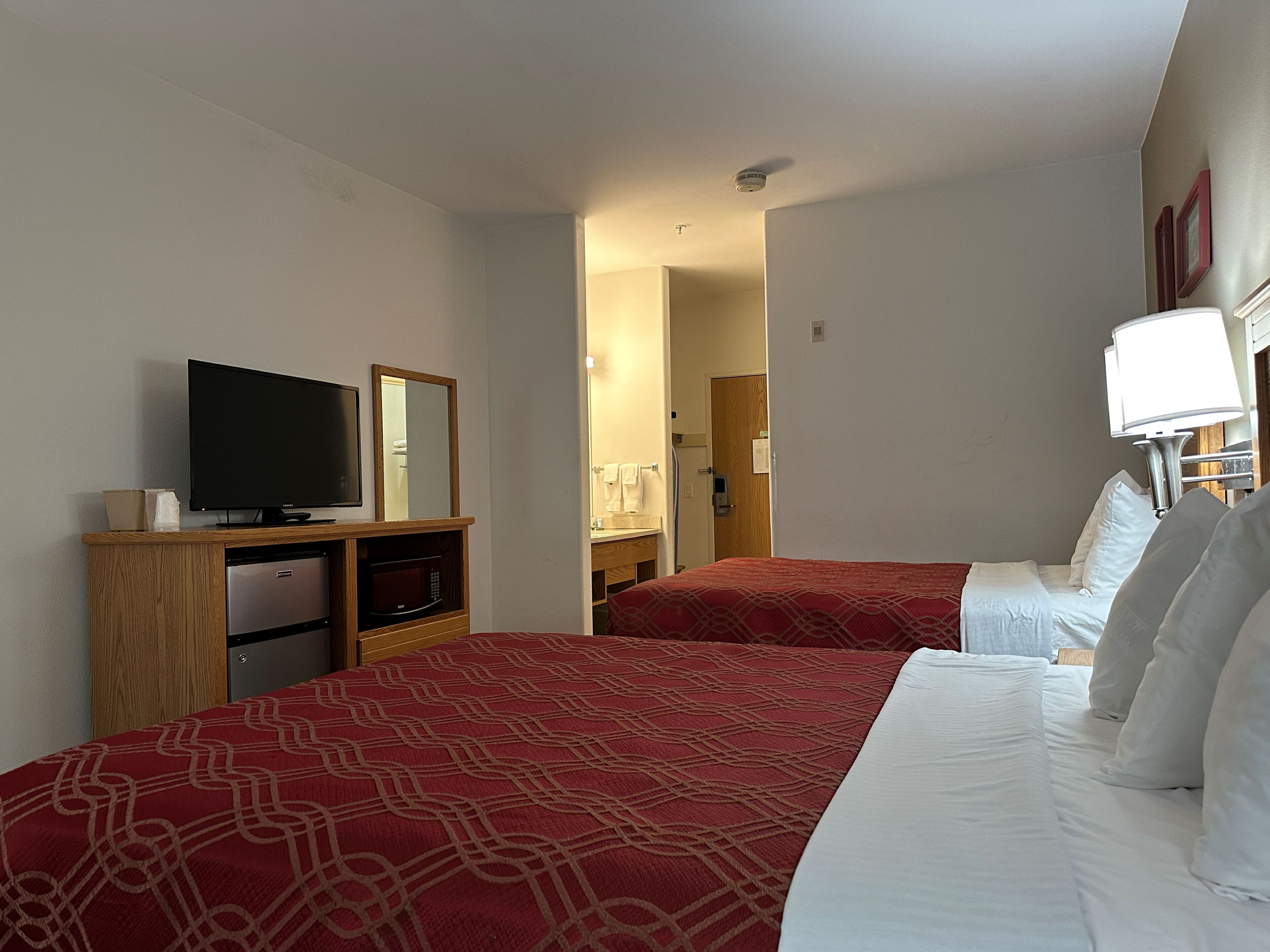 A hotel room with two beds, a television, a microwave, and a bathroom visible through an open door.