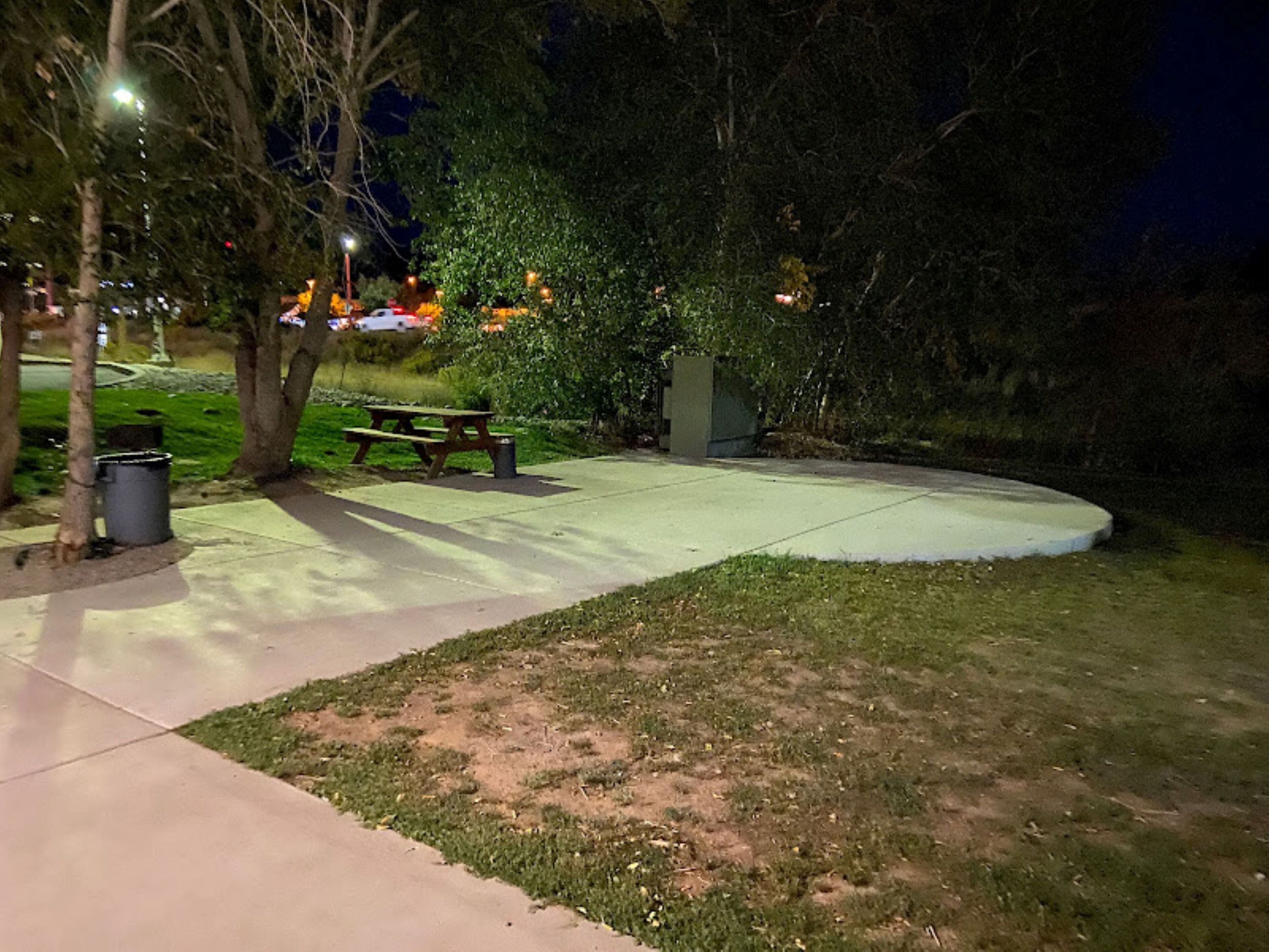 Un espace extérieur aménagé pour la nuit, comprenant une table de pique-nique, des bancs et une poubelle.