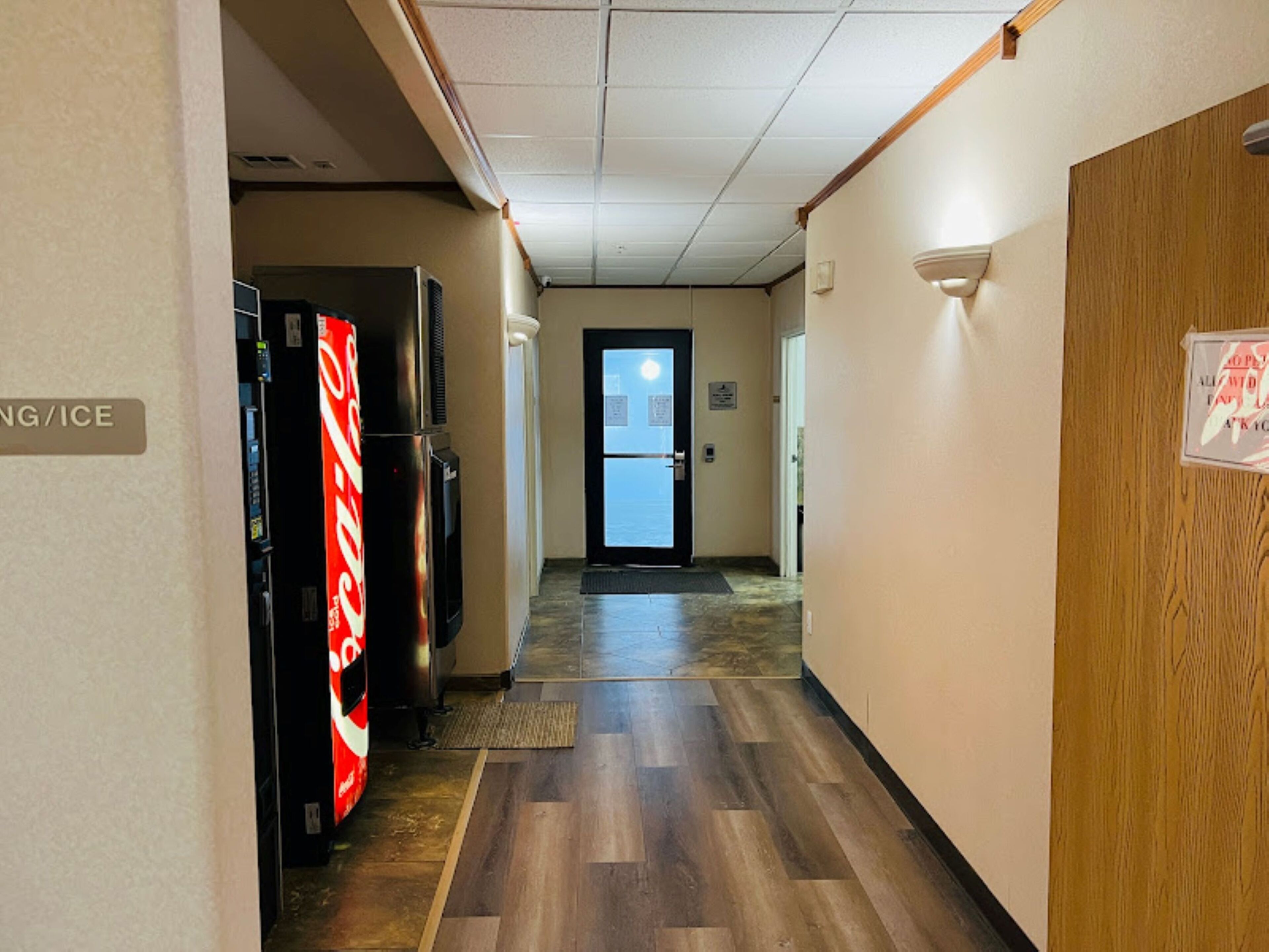 A hotel hallway with a Coca-Cola refrigerator, a door with a sign, and a wooden wall.