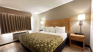 Hotellihuone, jossa on suuri sänky, yöpöytä lampun kanssa ja ikkuna, jossa on verhot.