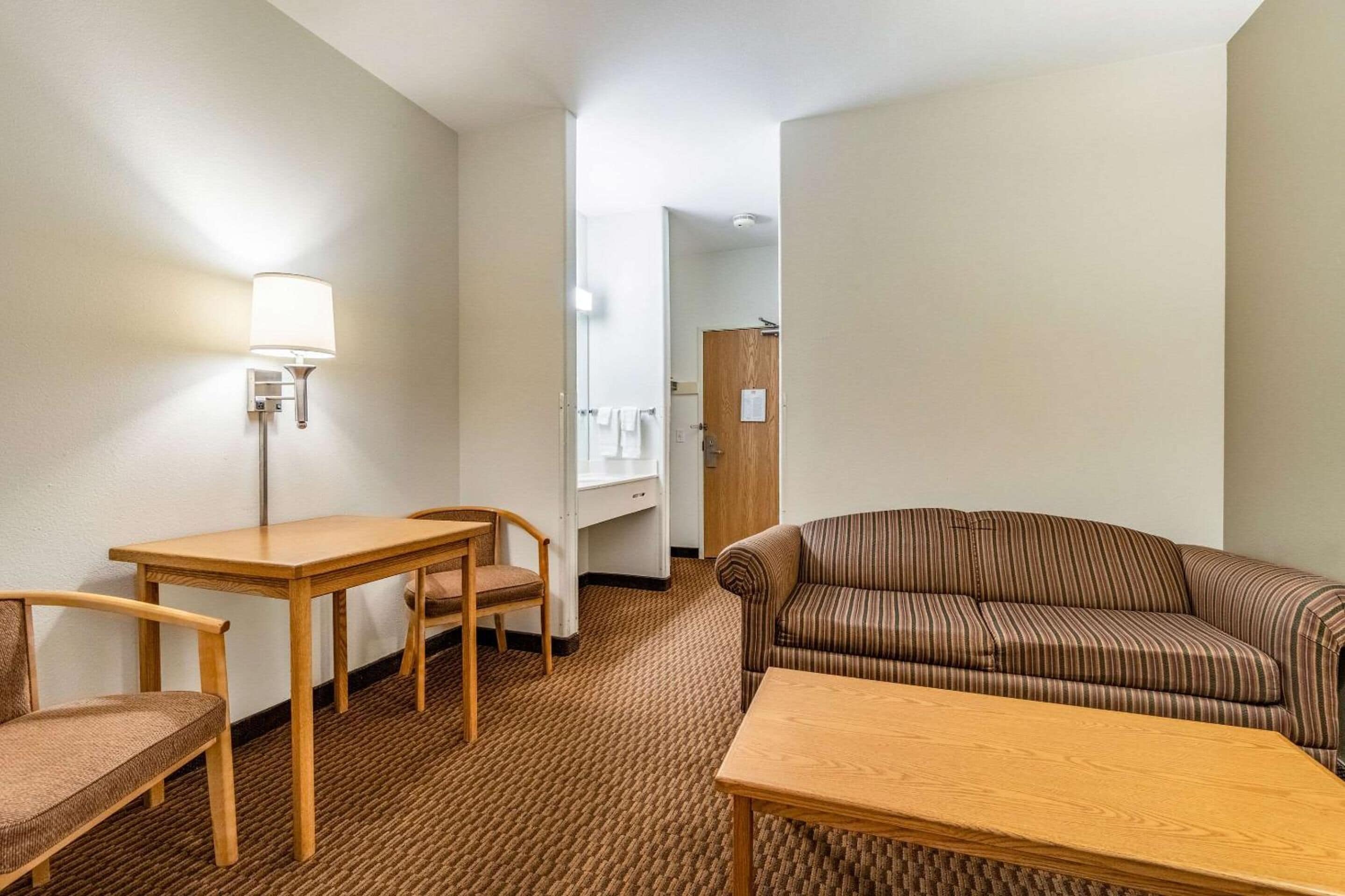 A hotel room with a wooden table, two chairs, a striped sofa, and a lamp.