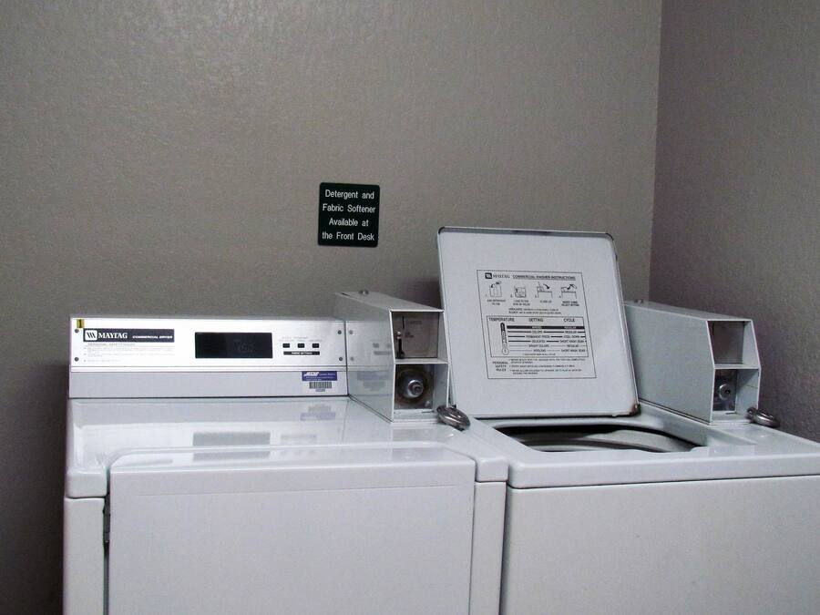 Lavadora de carga frontal con panel de control y un cartel en la pared que indica detergente y suavizante.