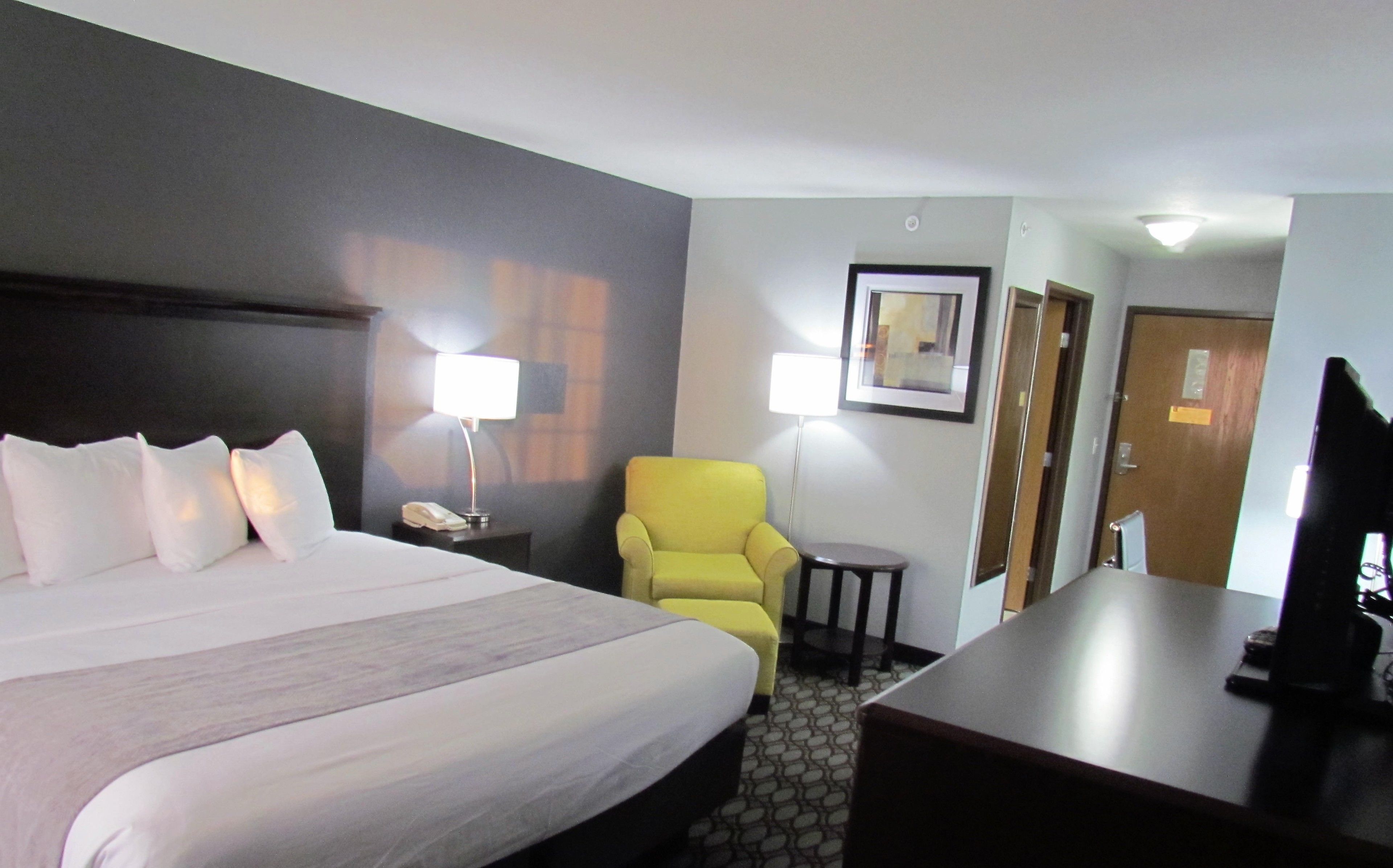 A hotel room with a large bed, a yellow armchair, a desk, and a television.
