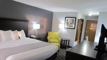 A hotel room with a large bed, a yellow armchair, a desk, and a television.