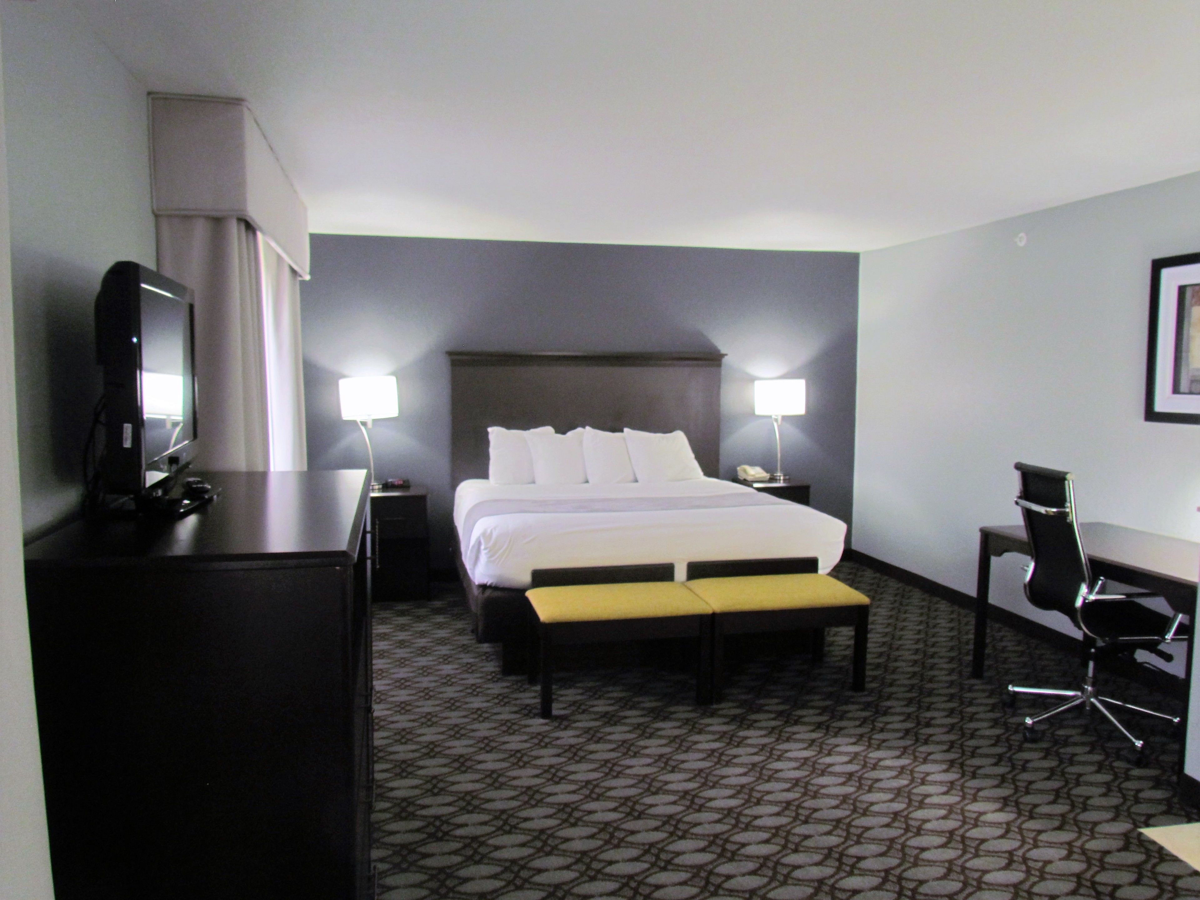 A hotel room with a bed, bedside lamps, a desk, a chair, and a television.