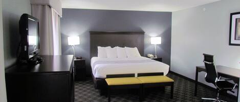 A hotel room with a bed, bedside lamps, a desk, a chair, and a television.
