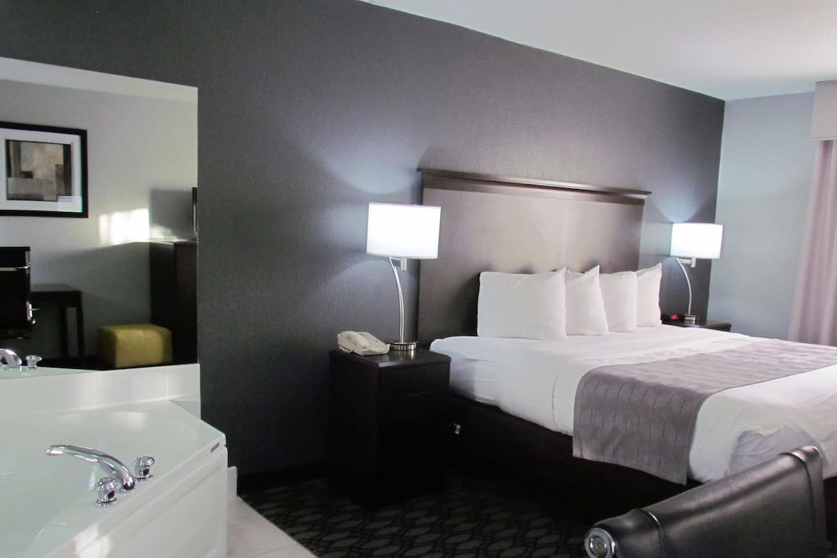 Habitación de hotel con una cama grande, dos lámparas de noche, una mesita de noche con teléfono, un espejo y una bañera.
