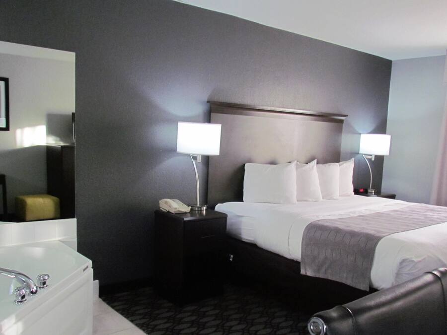 A hotel room with a large bed, two bedside lamps, a nightstand with a phone, a mirror, and a bathtub.