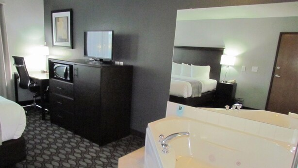 A hotel room with a large bed, a desk with a computer, a television, and a bathtub.