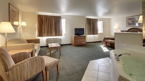 A hotel room with a sofa, armchair, small table, TV, dresser, and a bathtub.