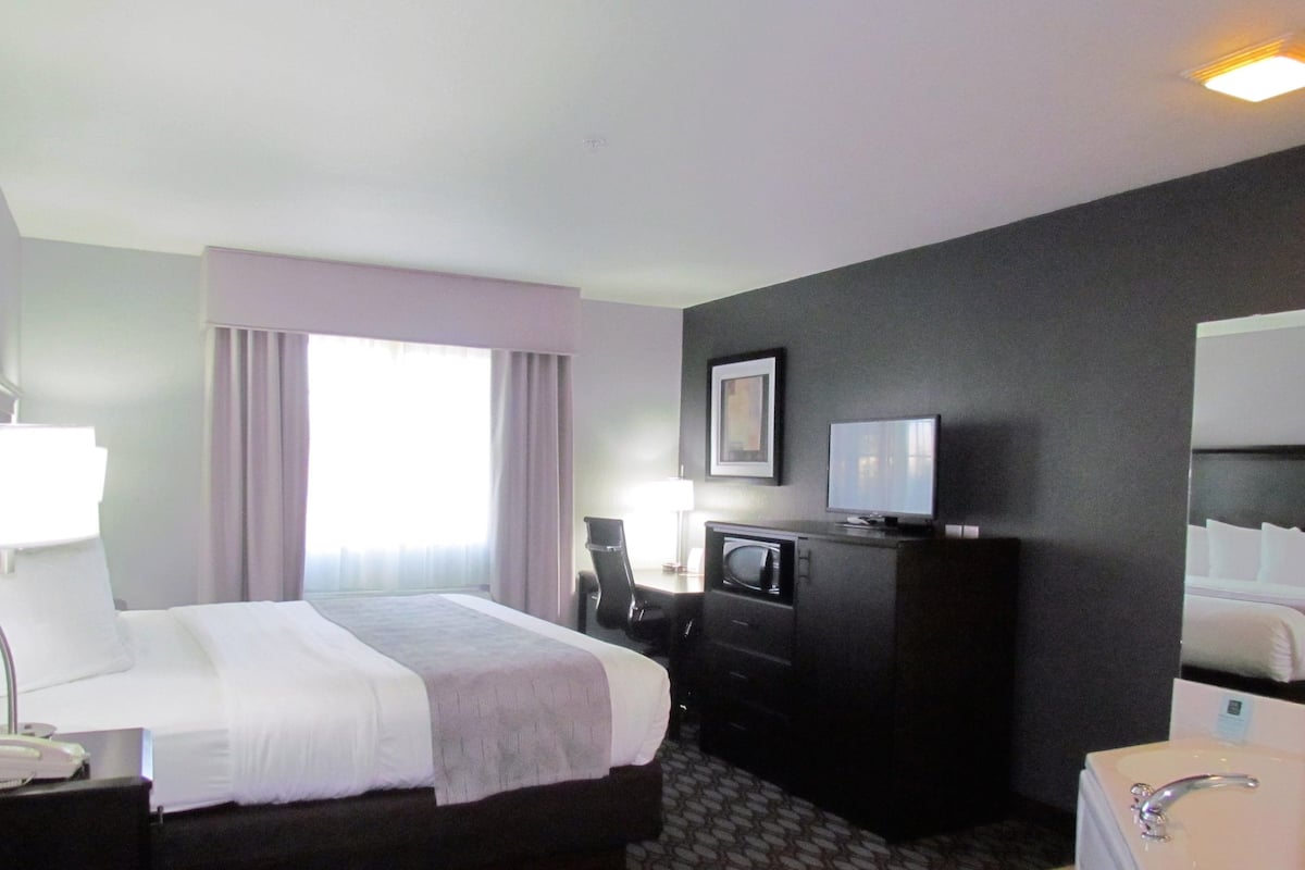 Habitación de hotel con cama, escritorio con lámpara, televisor y baño con lavabo y espejo.