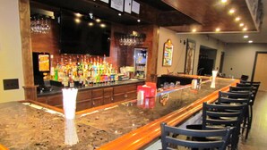 A bar area with a long counter, multiple bottles, glasses, and a few chairs.
