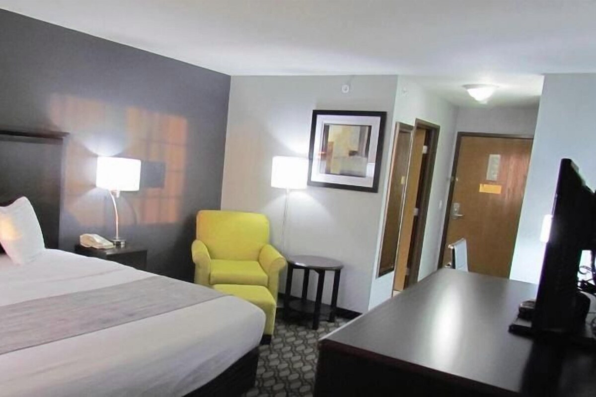 A hotel room with a large bed, a desk, a chair, a lamp, and a framed picture on the wall.