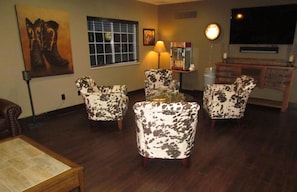 A living room with a wooden floor, a TV mounted on the wall, and a lamp on a table. - Oak Hill Inn & Suites (Canton)