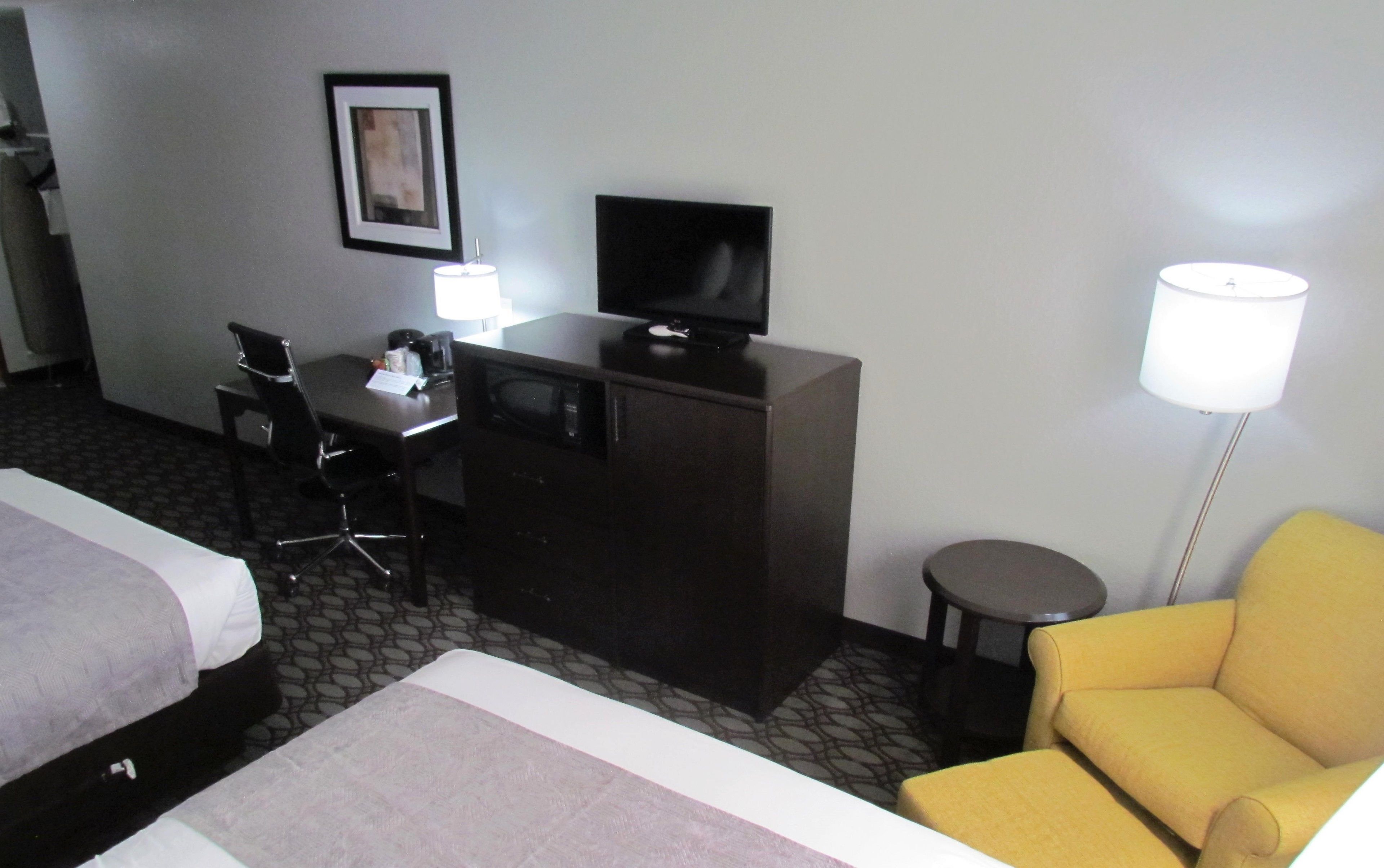 A hotel room with a bed, a desk with a computer, a television, a chair, and a lamp.