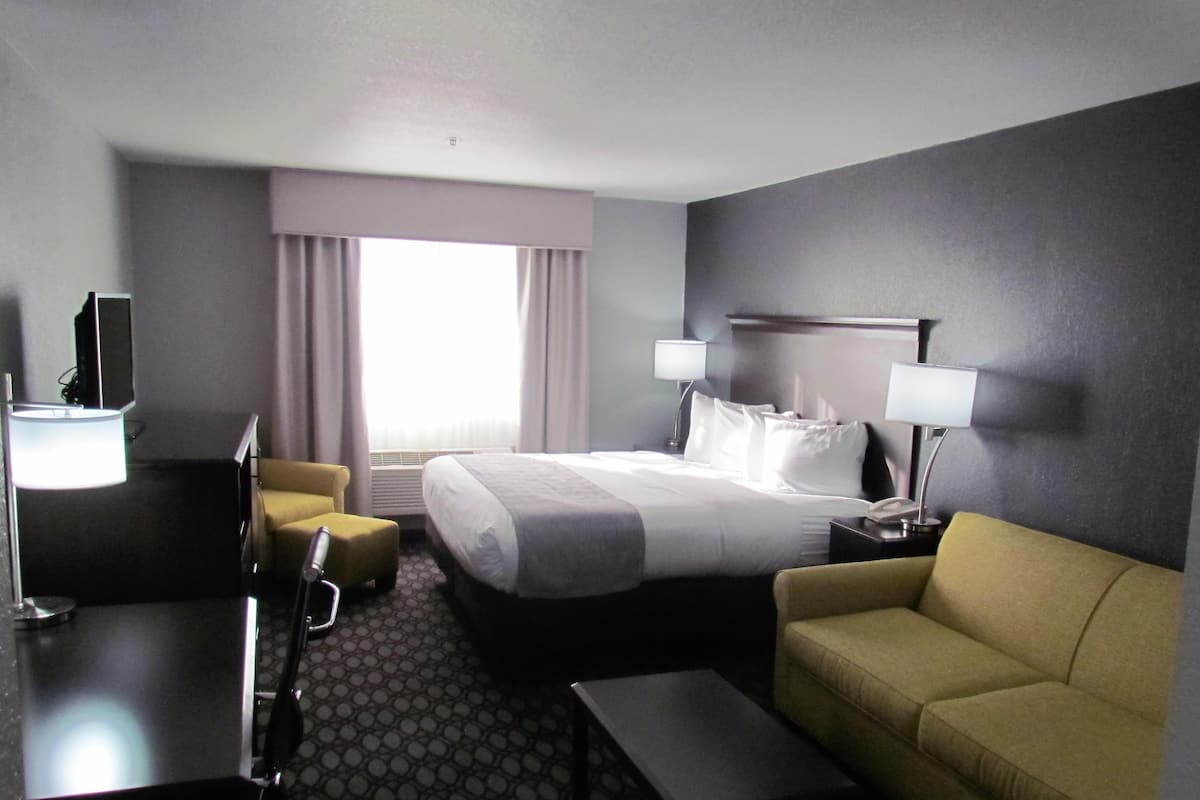 Habitación de hotel con cama, escritorio, sillón, sofá y lámpara.