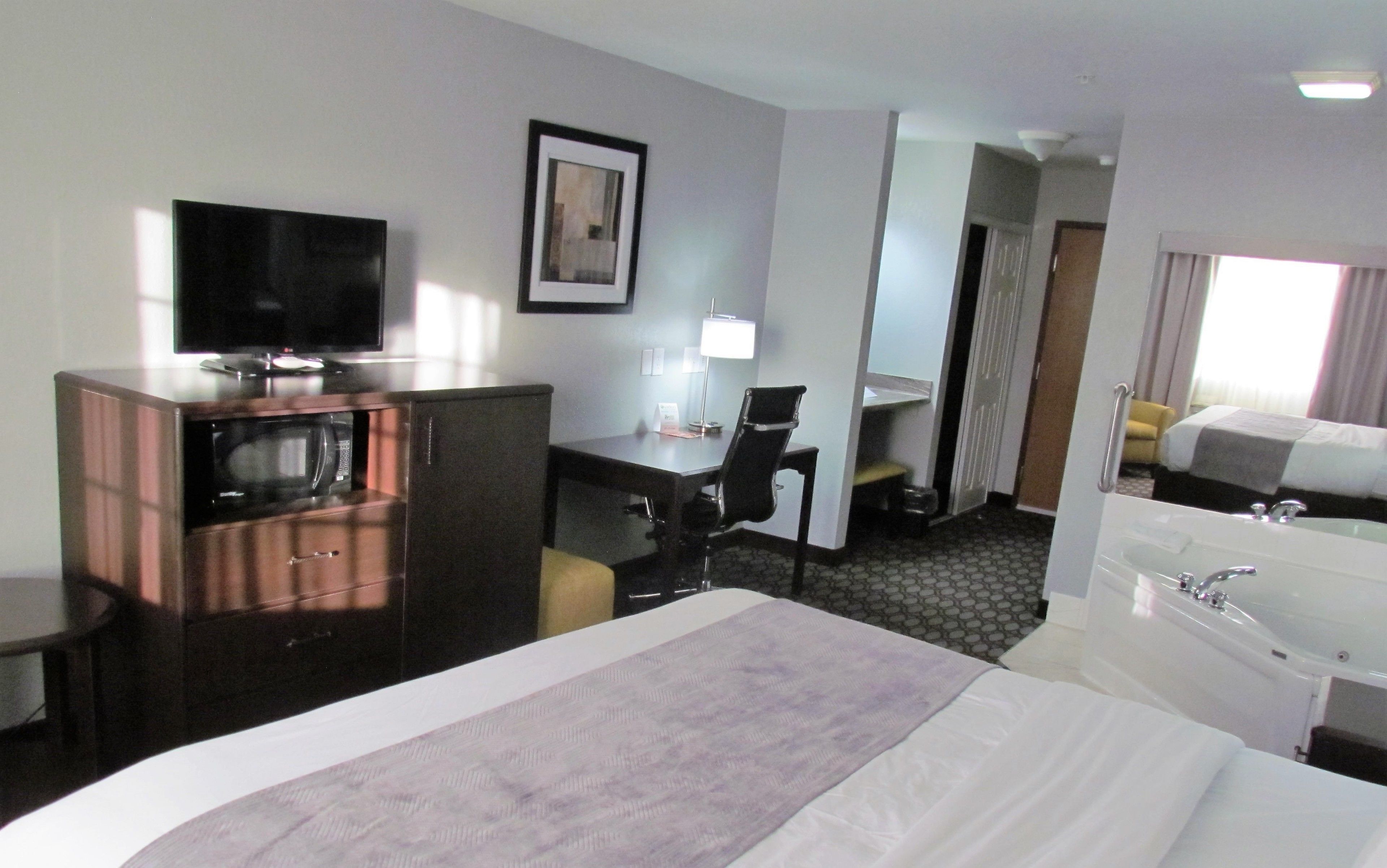 A hotel room with a bed, a desk, a TV, a lamp, and a bathroom.