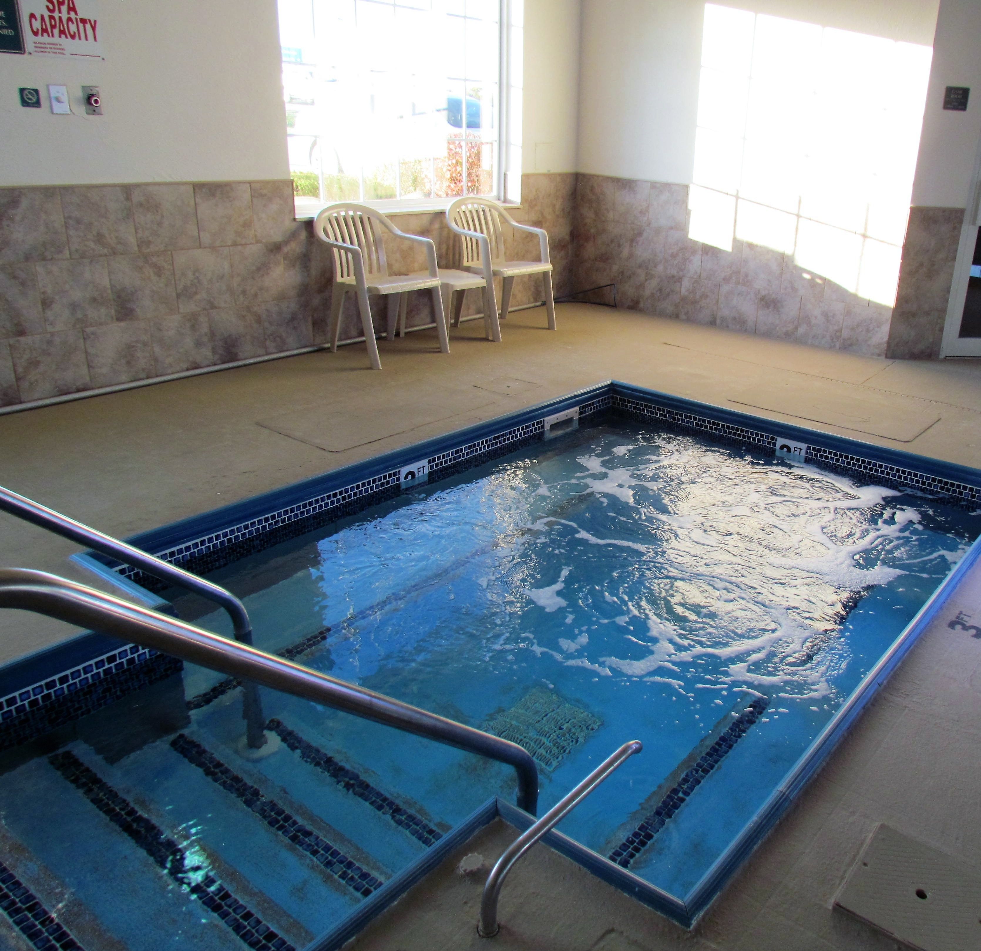 An indoor swimming pool with a tiled edge, a metal ladder, and two plastic chairs.