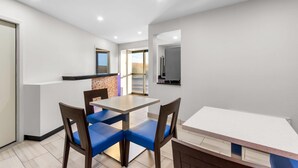 A modern kitchen with white cabinets, a countertop, and a sink. There is a dining area with a table and chairs.
