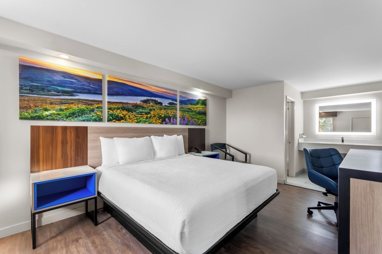 Una habitación de hotel moderna con una cama, un escritorio y una silla. Hay tres cuadros en la pared.