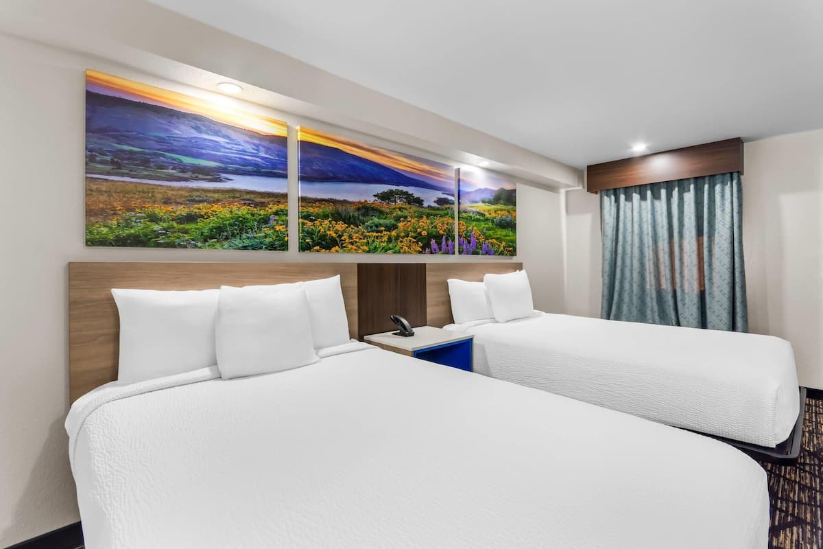A hotel room with two beds, a large landscape painting, a wooden headboard, a bedside table with a phone, and a patterned carpet.