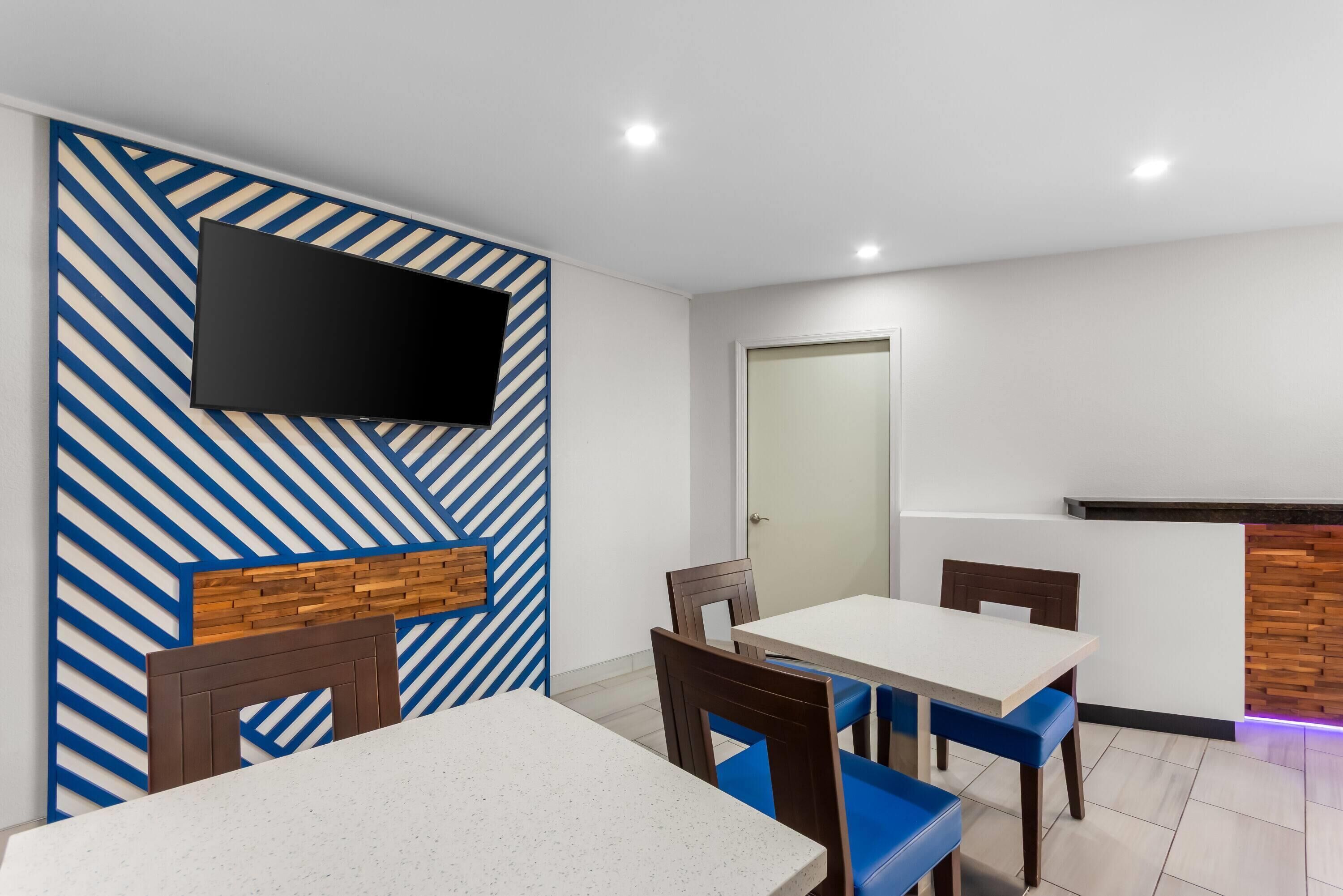 A modern dining area with a flat-screen TV mounted on a blue and white striped wall, wooden headboards, and blue cushioned chairs.