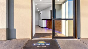 A hotel entrance with a glass door, a reception desk, and a doormat with the hotel's logo.