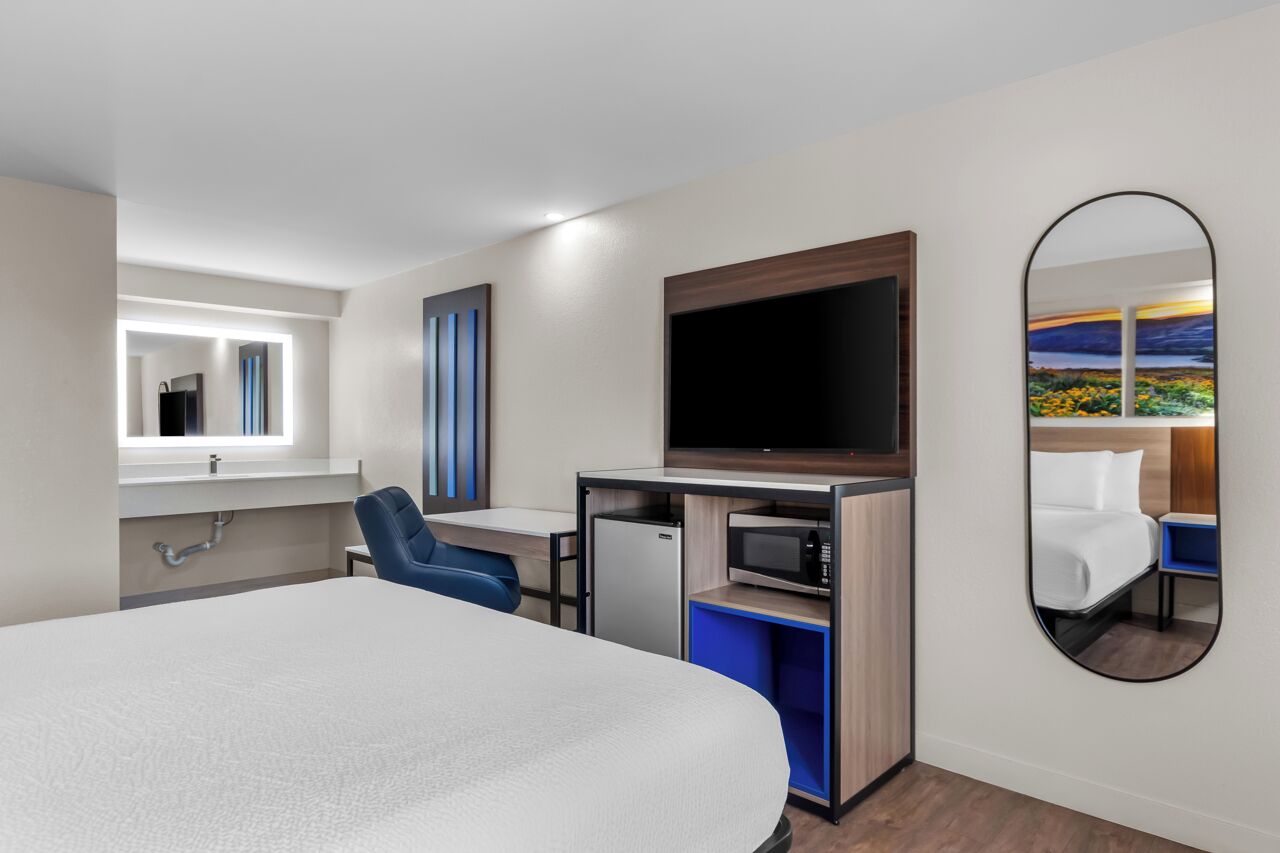 Hotelkamer met een bed, een bureau met stoel, een televisie, een magnetron en een grote spiegel.