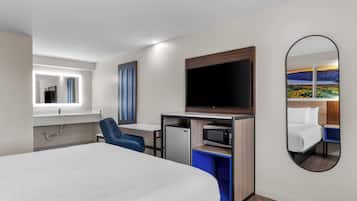 Hotelkamer met een bed, een bureau met stoel, een televisie, een magnetron en een grote spiegel.
