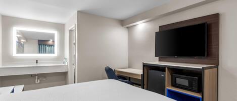 A hotel room with a bed, a desk with a chair, a television, and a microwave.