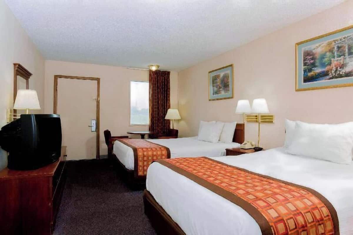 A hotel room with two beds, a television, a desk with a lamp, and a painting on the wall.
