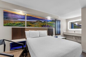 A modern hotel room with a large bed, a nightstand, a desk, and a large painting of a landscape. - Days Inn by Wyndham Indianapolis East Post Road (Indianapolis)