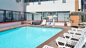 A swimming pool with lounge chairs and umbrellas, surrounded by a fenced patio area.