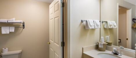 A bathroom with a toilet, a sink, a mirror, and towels on a rack.