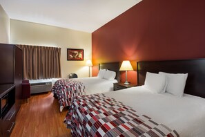 Ein Hotelzimmer mit zwei Betten, einem Schreibtisch, einem Sessel, einem Fernseher und einem Bild an der Wand.