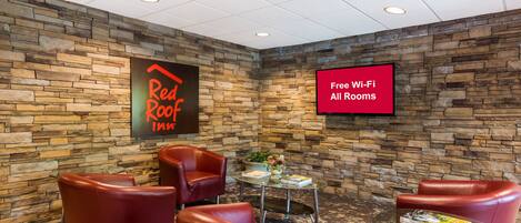 A hotel lobby with stone walls, leather chairs, a glass table, and a TV screen advertising free Wi-Fi.