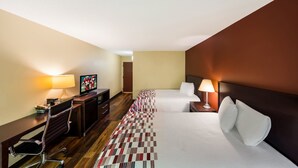 Une chambre d’hôtel comprenant un lit, un bureau avec une chaise, une télévision et deux lampes de chevet.