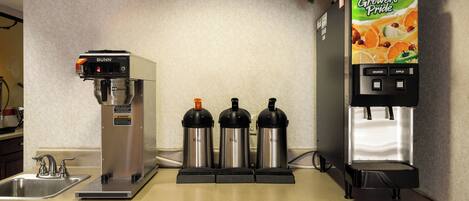 Una estación de café con una máquina de café Bunn, tres tazas térmicas y un dispensador de jugo.