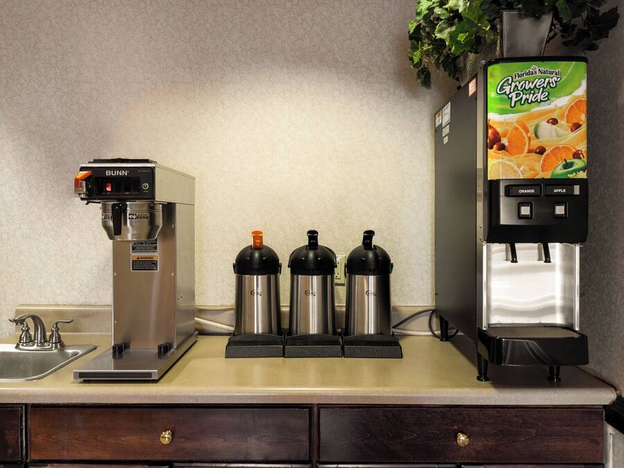 A coffee station with a Bunn coffee machine, three insulated mugs, and a juice dispenser.
