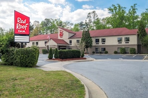 Un hôtel Red Roof Inn, reconnaissable à son grand panneau, son parking et son bâtiment à toit rouge.