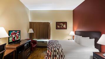Habitación de hotel con cama, dos lámparas de noche, televisor sobre un escritorio, una silla, ventana con cortinas e imagen enmarcadas en la pared.